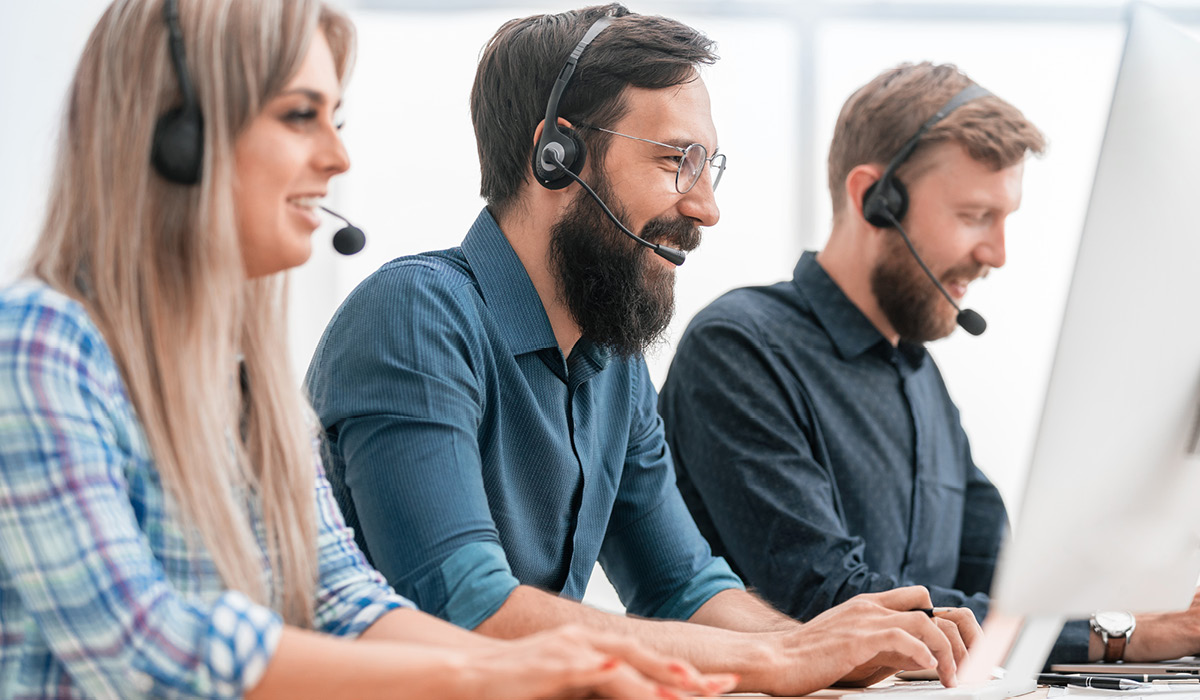 Three customer support professionals smile at their computer screens whilst wearing headsets.